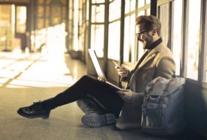 Support image (man on laptop and phone) depicting remote worker communicating as part of remote teams for technical creatives.